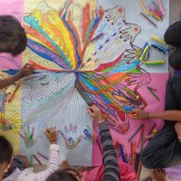 Séance de groupe filles-garçons. Réalisation d'un mandala mains pour rassembler les différences de chacun. Travail réalisé au sol sur un support commun construit ensemble.